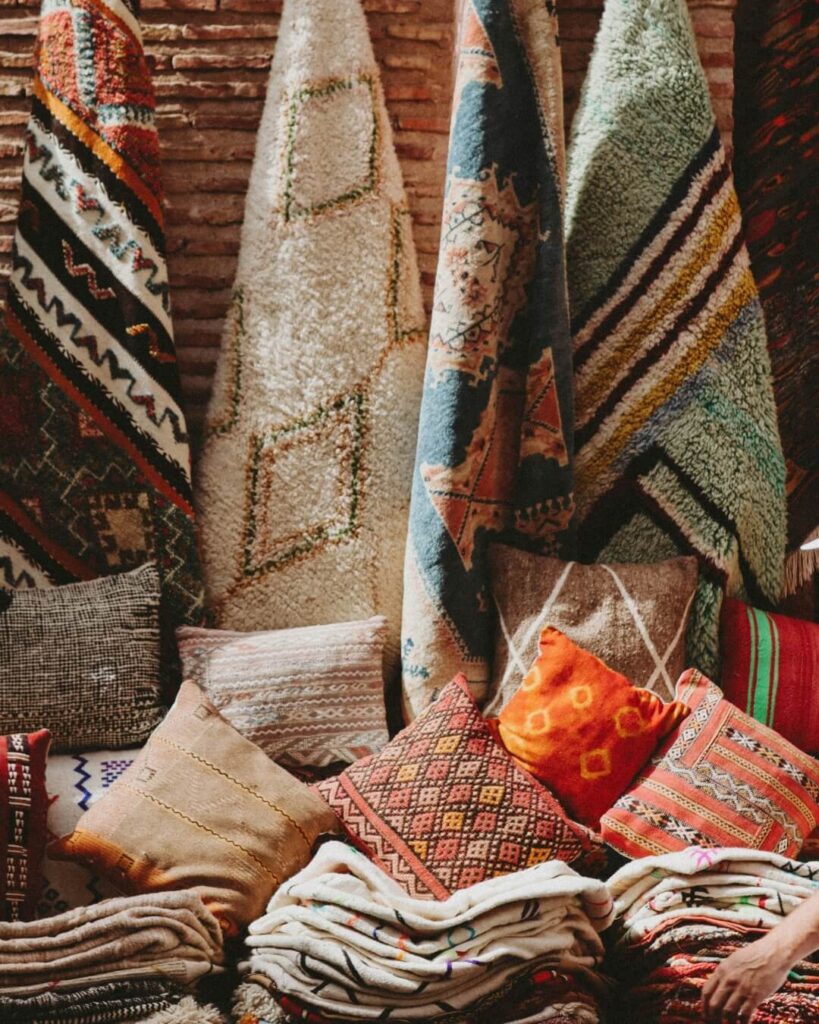 Folded linens, pillows, and hanging hugs on display at a market in Morocco.