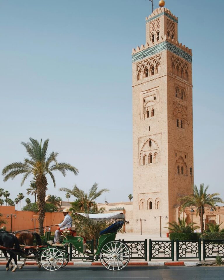 Kutubiyya Mosque in Marrakesh, surrounded by palm trees and a horse-drawn carriage.