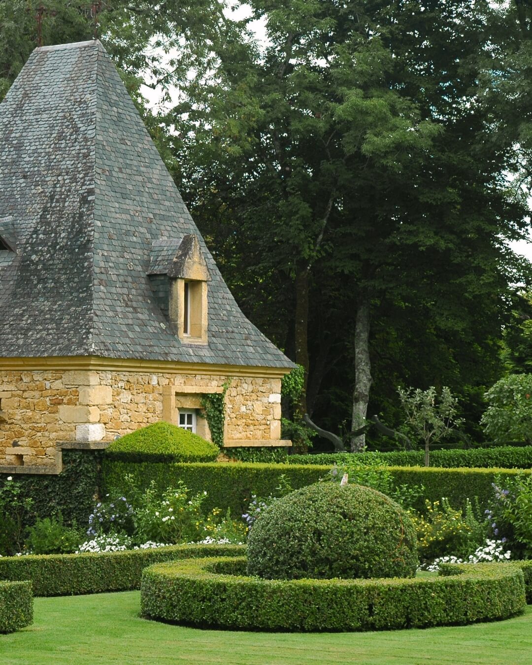 Stone pavilion in a manicured Dordogne garden with geometric hedges and lush grass.