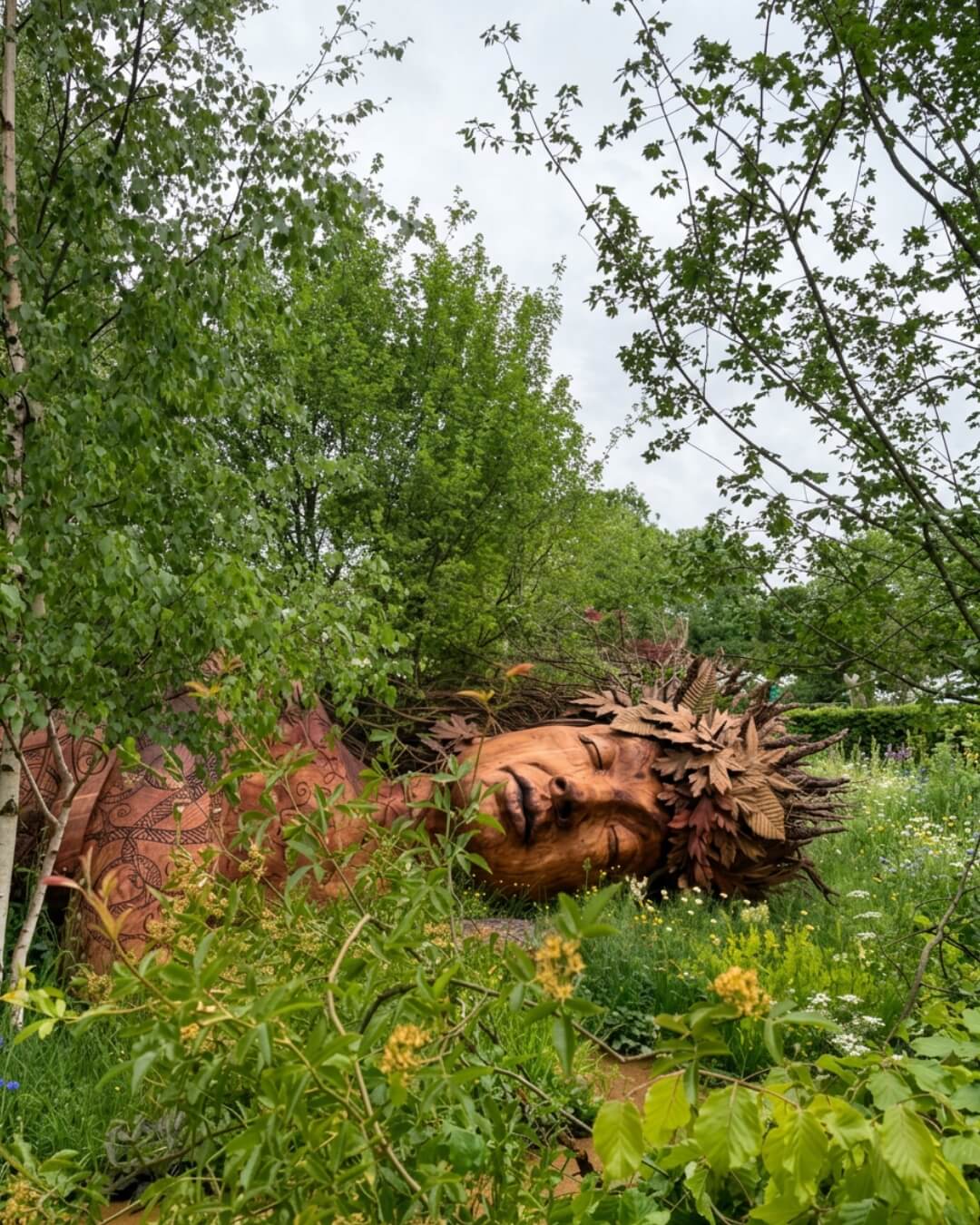 Wood sculpture of a resting nymph among lush green forest grounds at the Chelsea Garden Show in England.