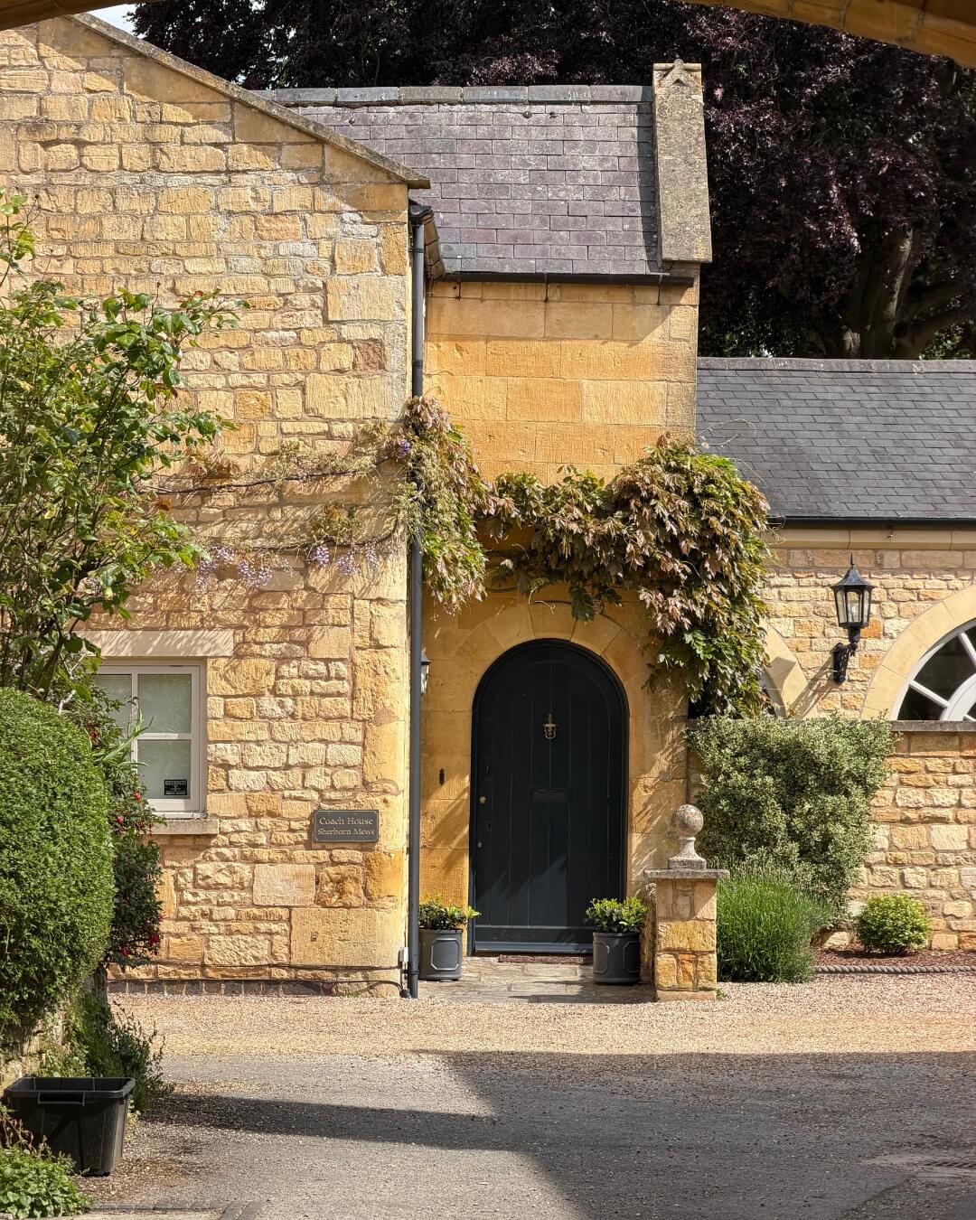 Historic stone home exterior in Chipping Camden, Gloucestershire, England featuring manicured hedges and climbing ivy.