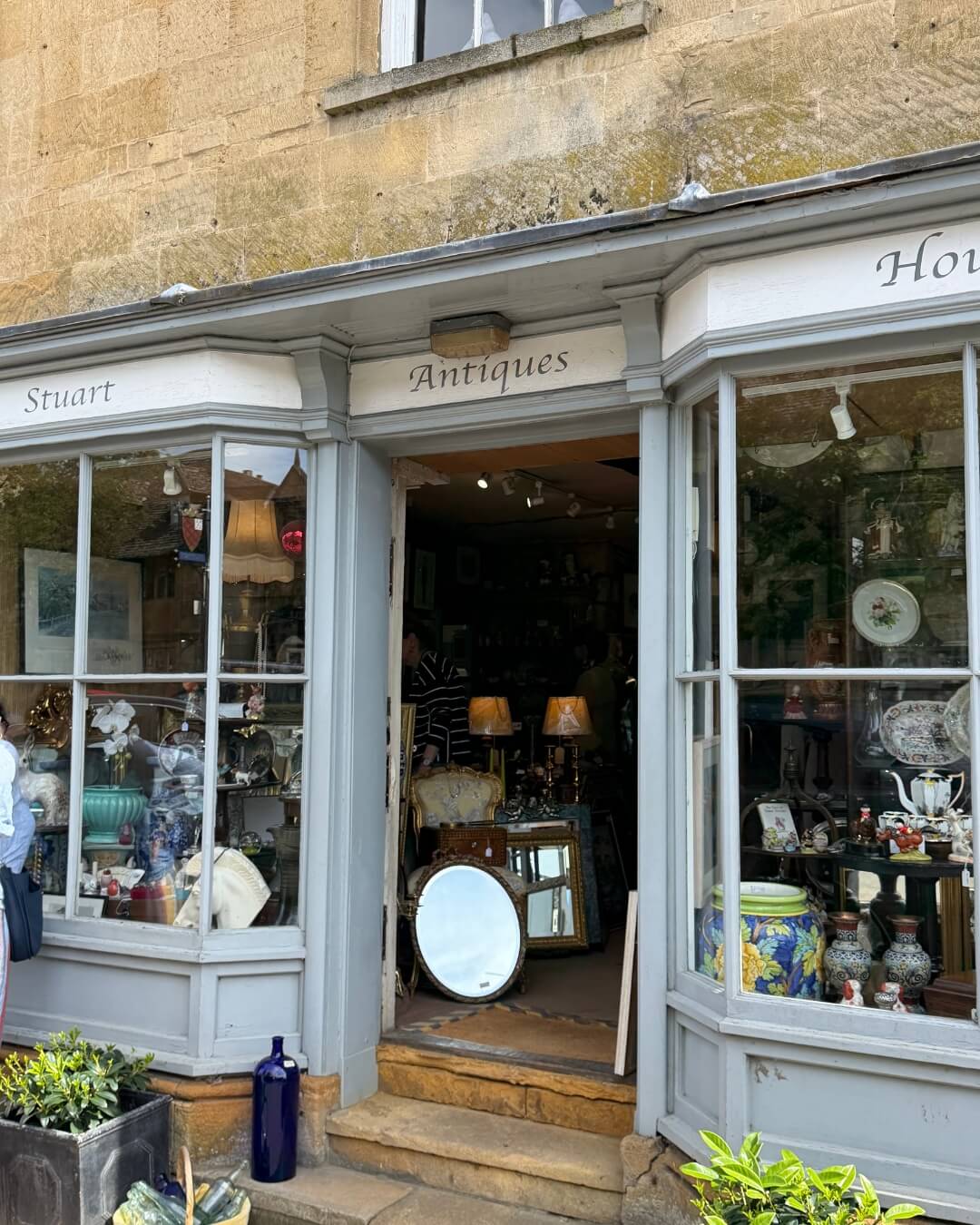 Stuart House Antiques exterior with vintage goods displayed behind large glass windows in Chipping Camden, England.
