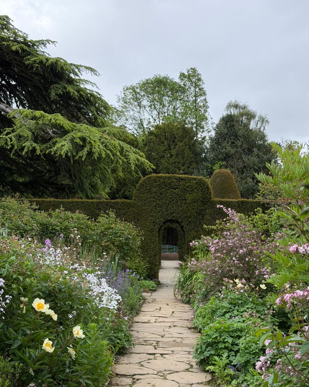 A stone garden path framed by lush flower beds and green hedge archways at Hidcote Manor Garden.