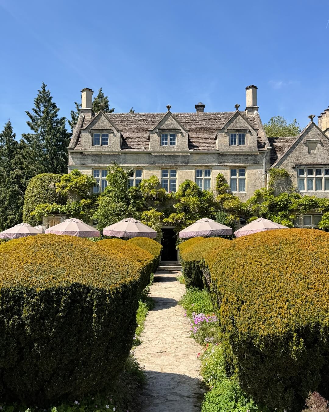 THE PIG-in the Cotswolds historic stone estate and boutique hotel with an umbrella shaded terrace and lush hedges.