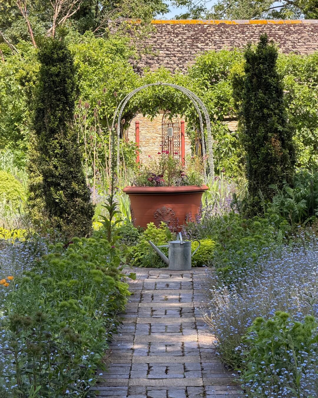 The Pig-in the Cotswolds wild flower garden, featuring a walking path and a large terracotta planter.