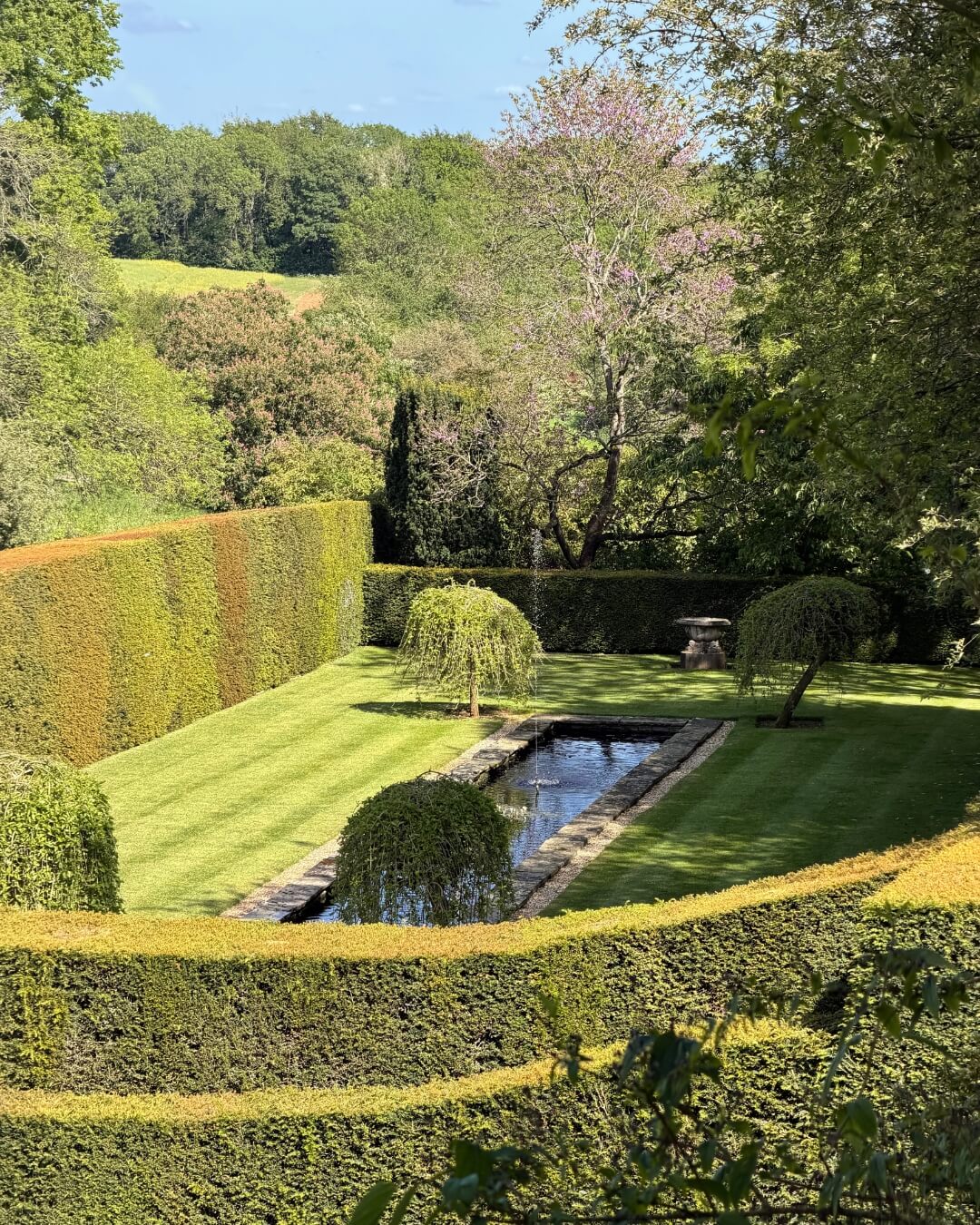 Upton Wold garden with manicured hedges surrounding a stone garden pond in Blockley, England.