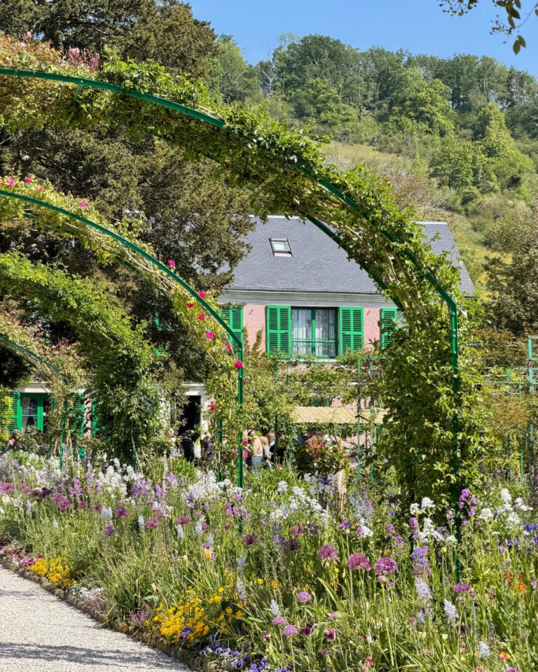 Claude Monet's Giverny home and garden in Normandy, France featuring purple and yellow flowers along the walking path and rose bushes along green arches.