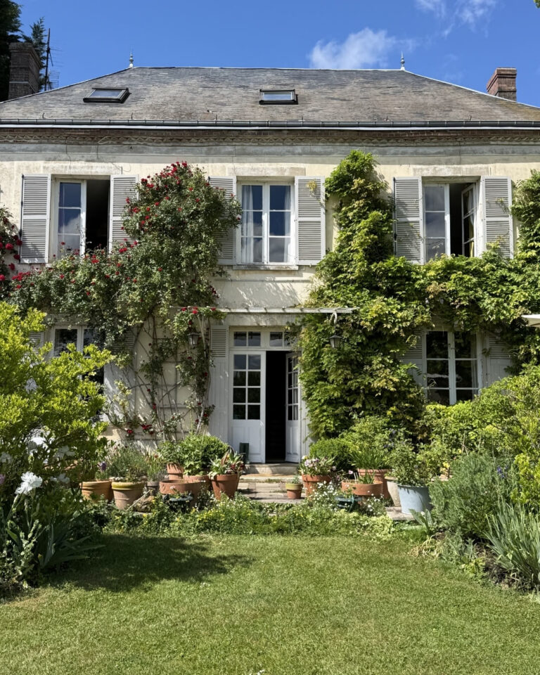 Home exterior in Normandy, France with a lush green garden and climbing ivy.