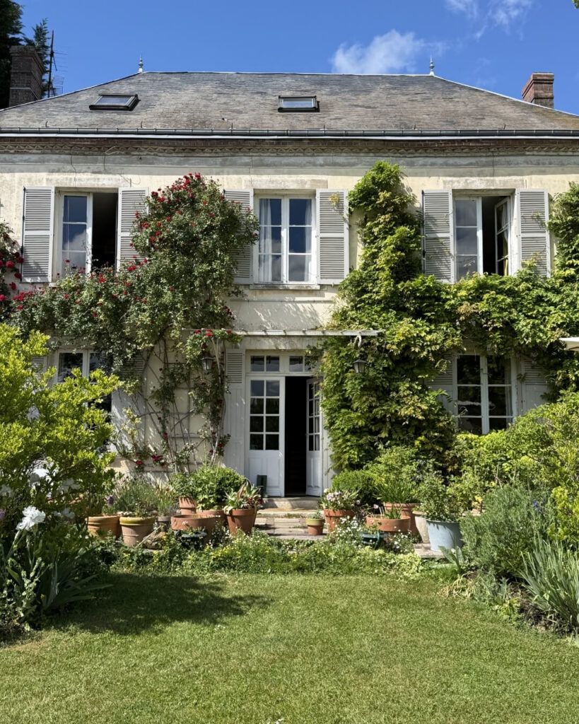 Home exterior in Normandy, France with a lush green garden and climbing ivy.