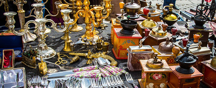 Table display of French antique coffee grinders, cutlery, and candlestick holders at an open market along the French Riviera.