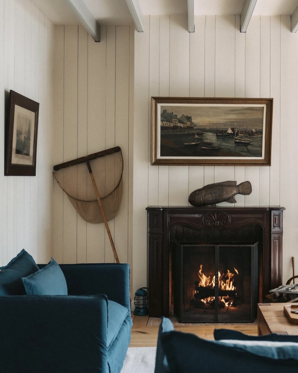 Maisons de Bricourt salon interior with an open fireplace, plush chairs, and vintage fishing themed decor.