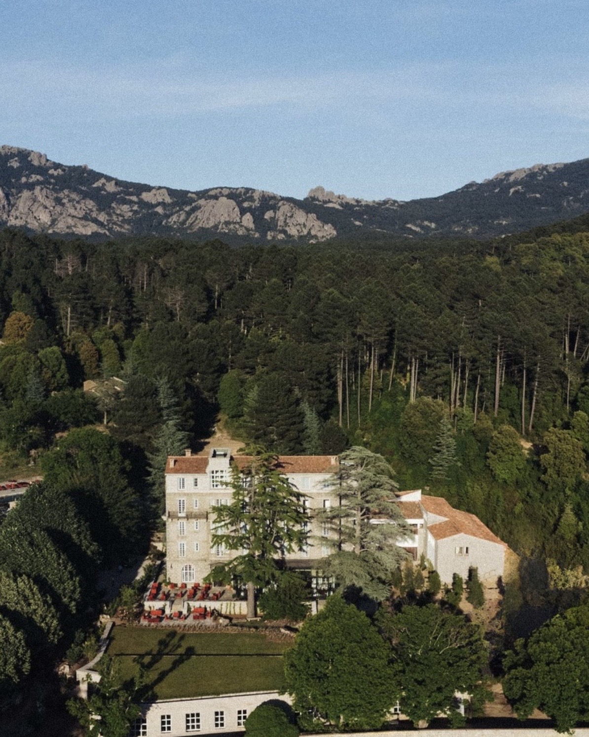 Domaine Le Mouflon D'Or estate exterior with lush surrounding trees and rocky mountains in the distance.