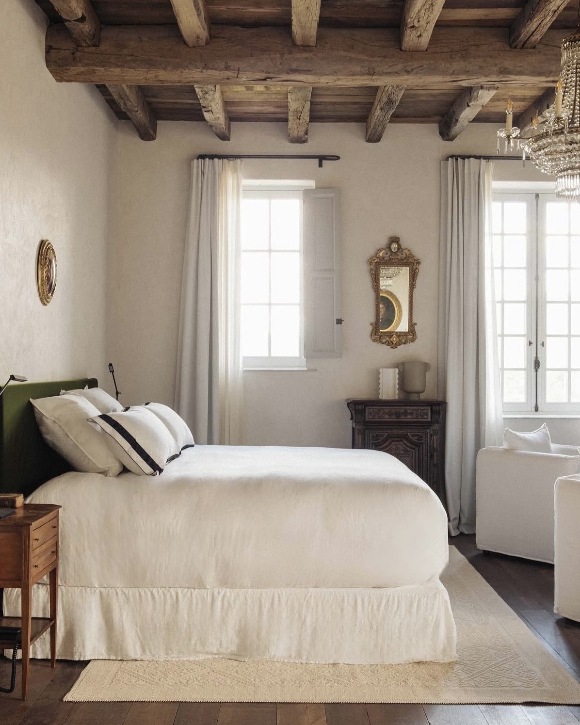 Domaine Le Mouflon D'Or boutique hotel interior with a plush bed in white linens, rustic exposed beams, and a crystal chandelier.