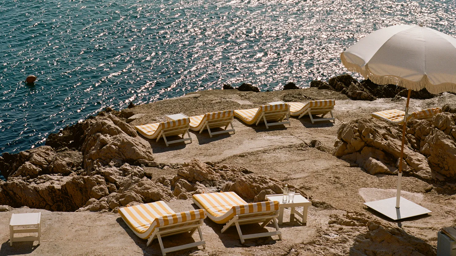 Lounge chairs and white parasols positioned along the rocky Mediterranean Sea at the Tuba Club in Marseille.