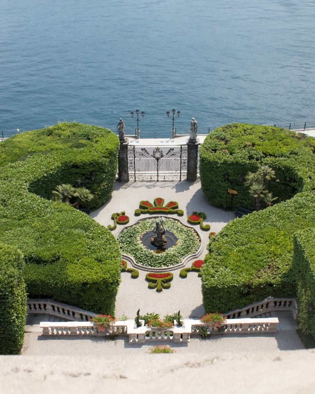 Manicured hedges and garden pond featuring red flowers along the edge of Lake Como in Italy.