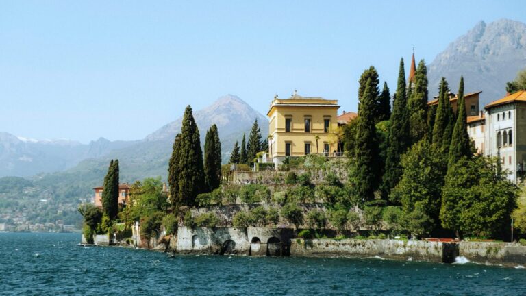 View of estates, cypress trees, and mountains along Lake Como, Italy.
