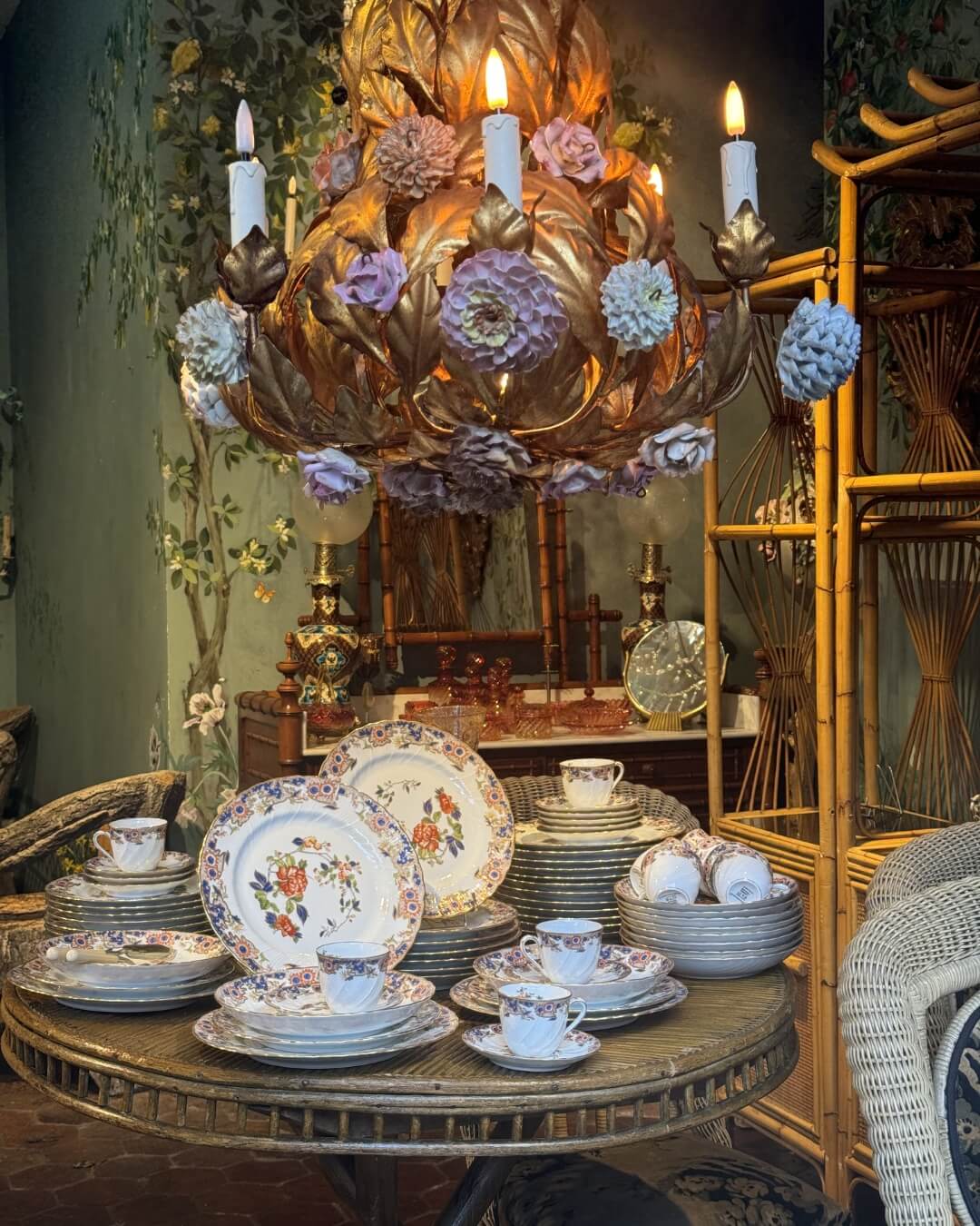Parisian antique store with an ornate floral and gold chandelier above vintage china and wicker chairs.