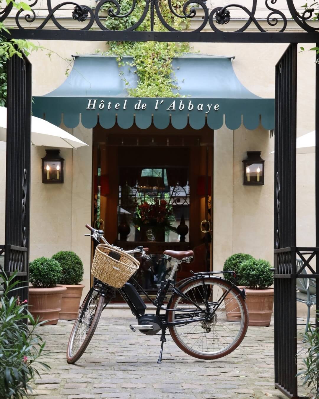 Hotel de l'Abbaye entrance framed by iron gates and a bicycle with a basket in Paris, France.