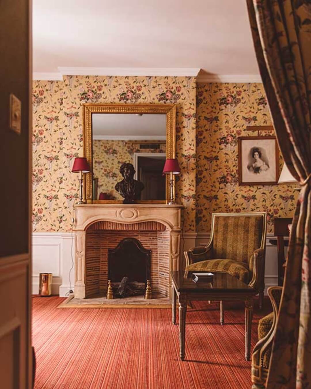 French boutique hotel room interior with antique furniture, framed art, and floral wallpaper.