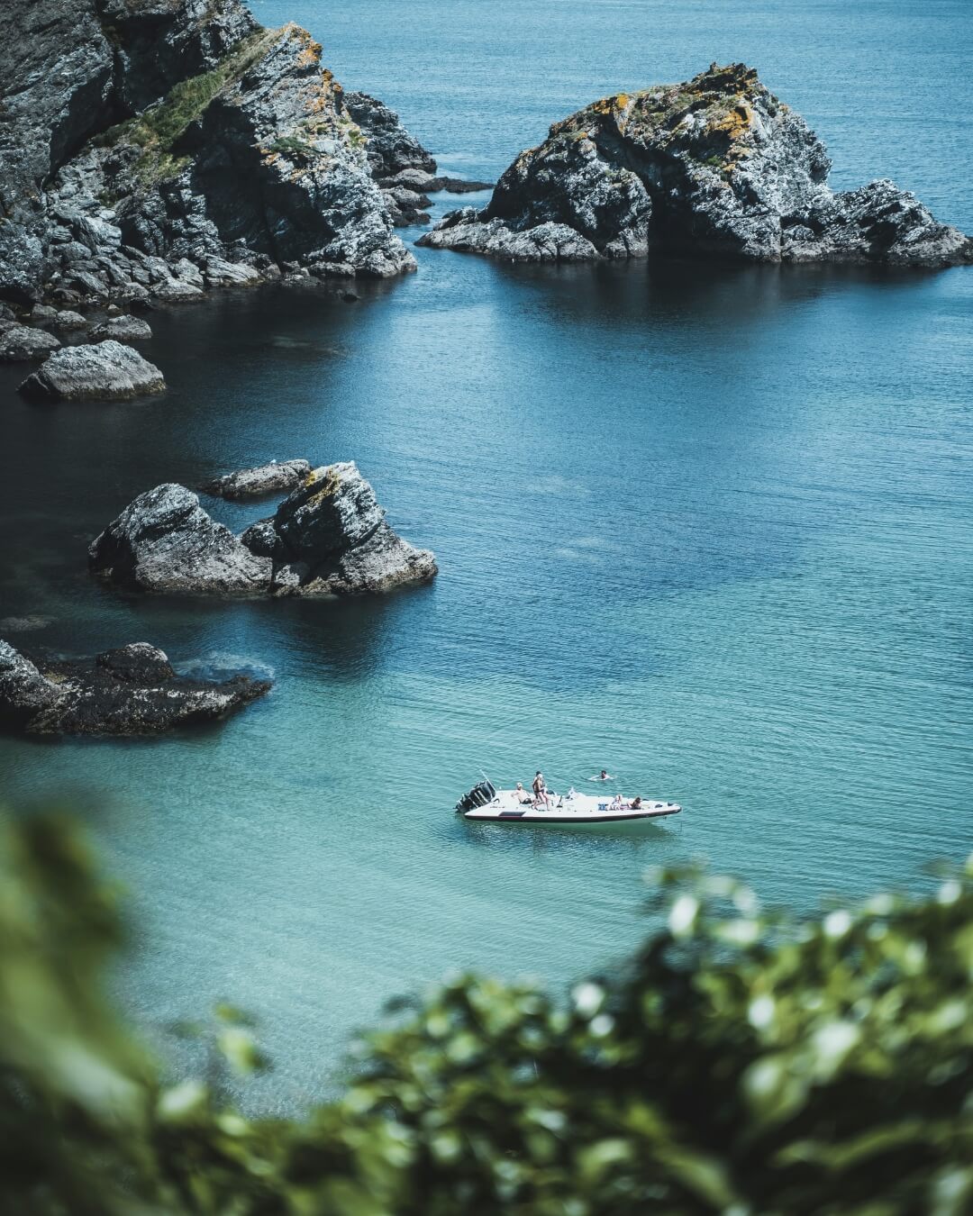 View of the rocky coast of Belle Île en Mer with a white boat moored near the shore.