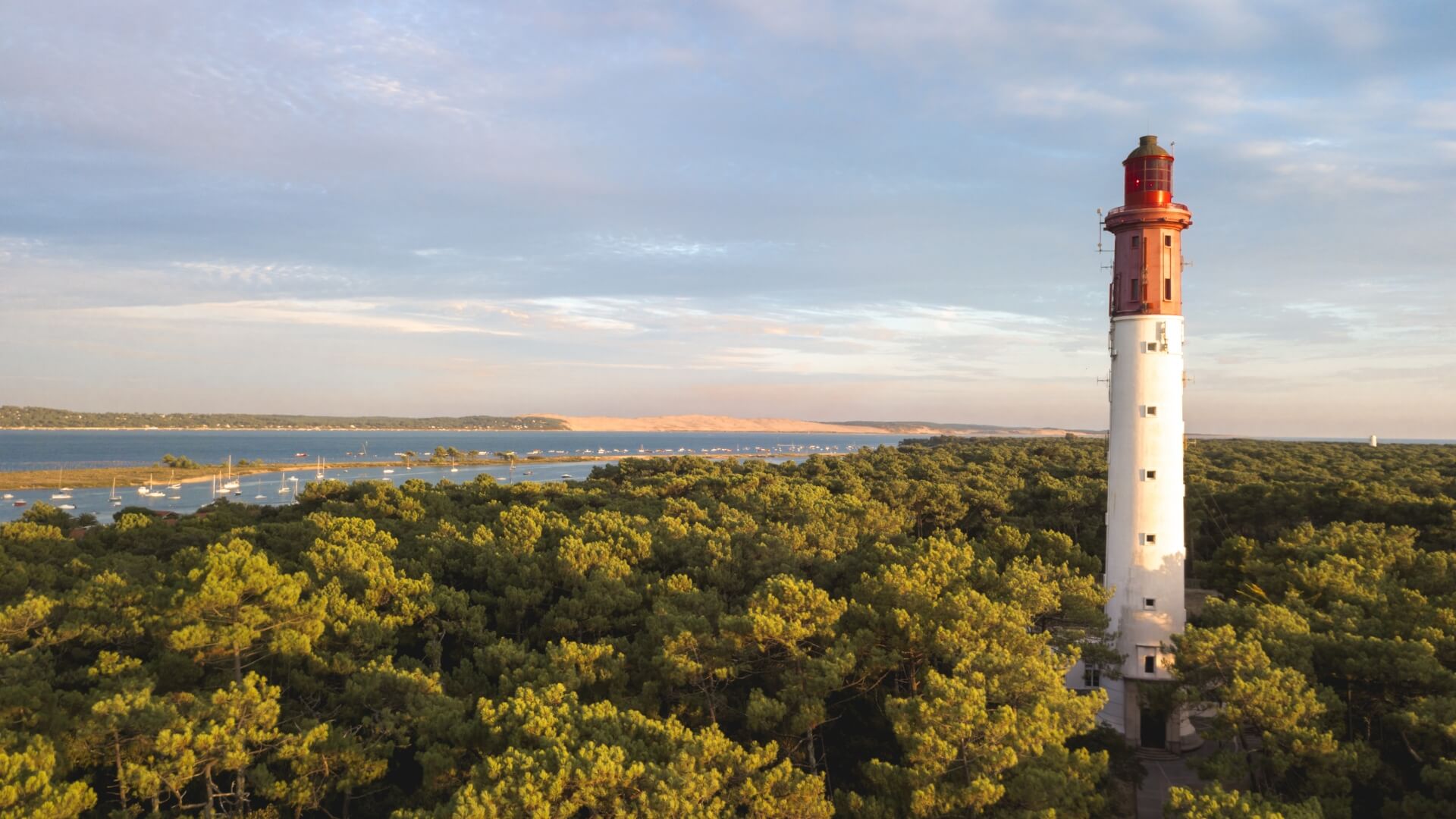 View of the Cap Ferret Atlantic coastline with lush green trees surrounding a white and red light house.