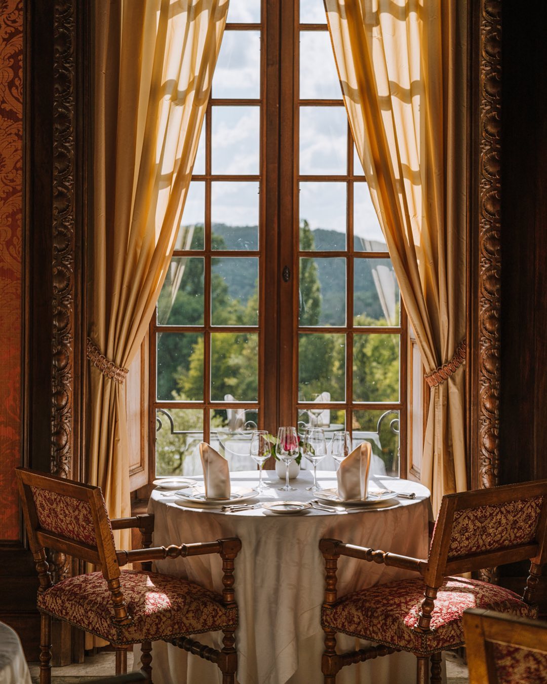 Chateau de la Treyne dining room interior with an intimate table set with two antique chairs facing French windows.
