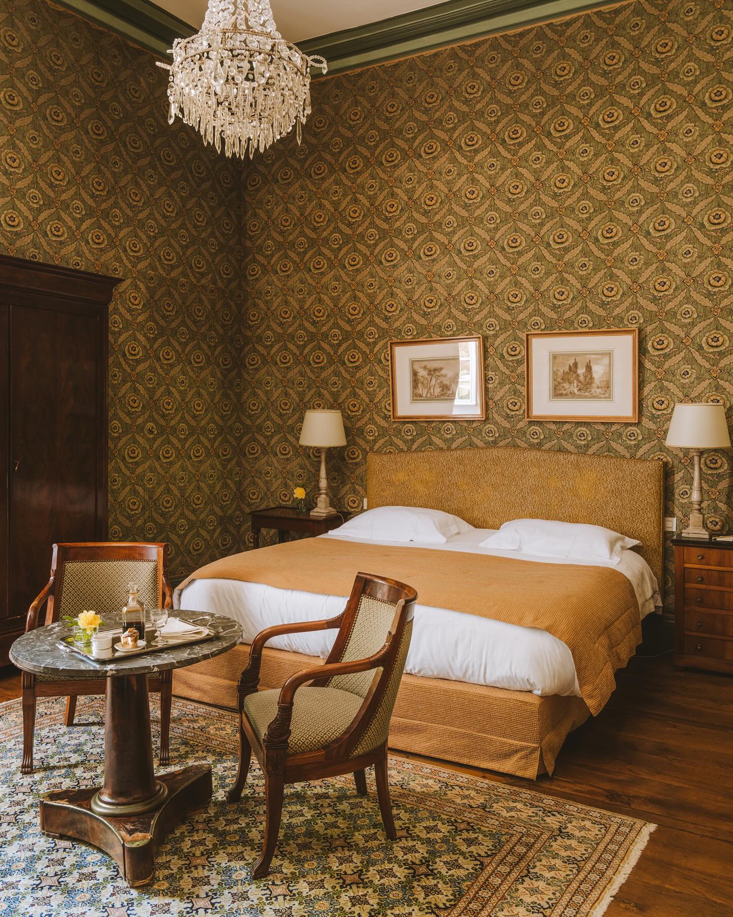 Chateau de la Treyne luxury hotel room with patterned wallpaper, a crystal chandelier, and a plush made bed.