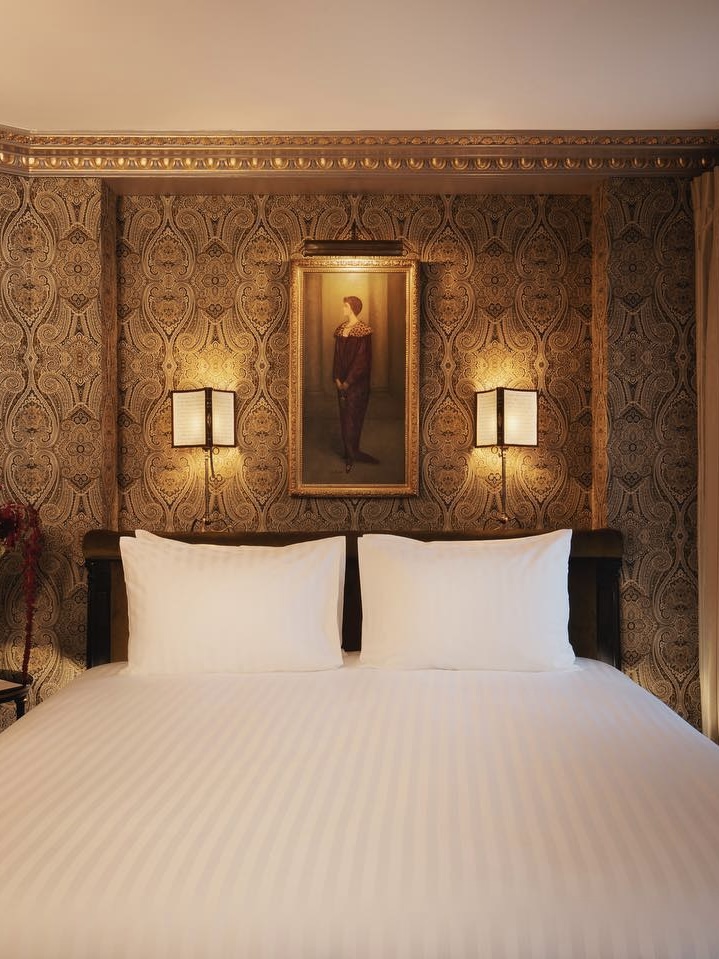 Maison Proust luxury hotel room interior with patterned wallpaper, soft bedside lighting, and crispy white sheets.