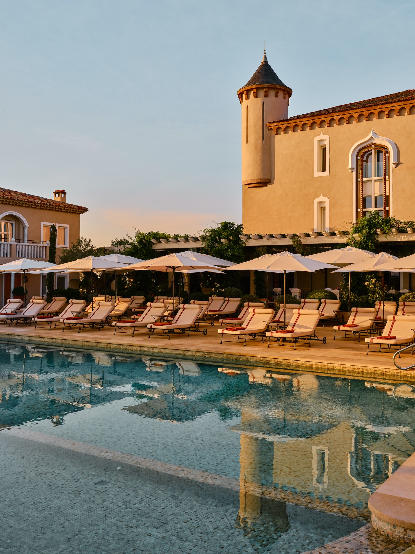Tiled swimming pool at Château de la Messardière in Saint Tropez, surrounded by lounge chairs and white umbrellas.