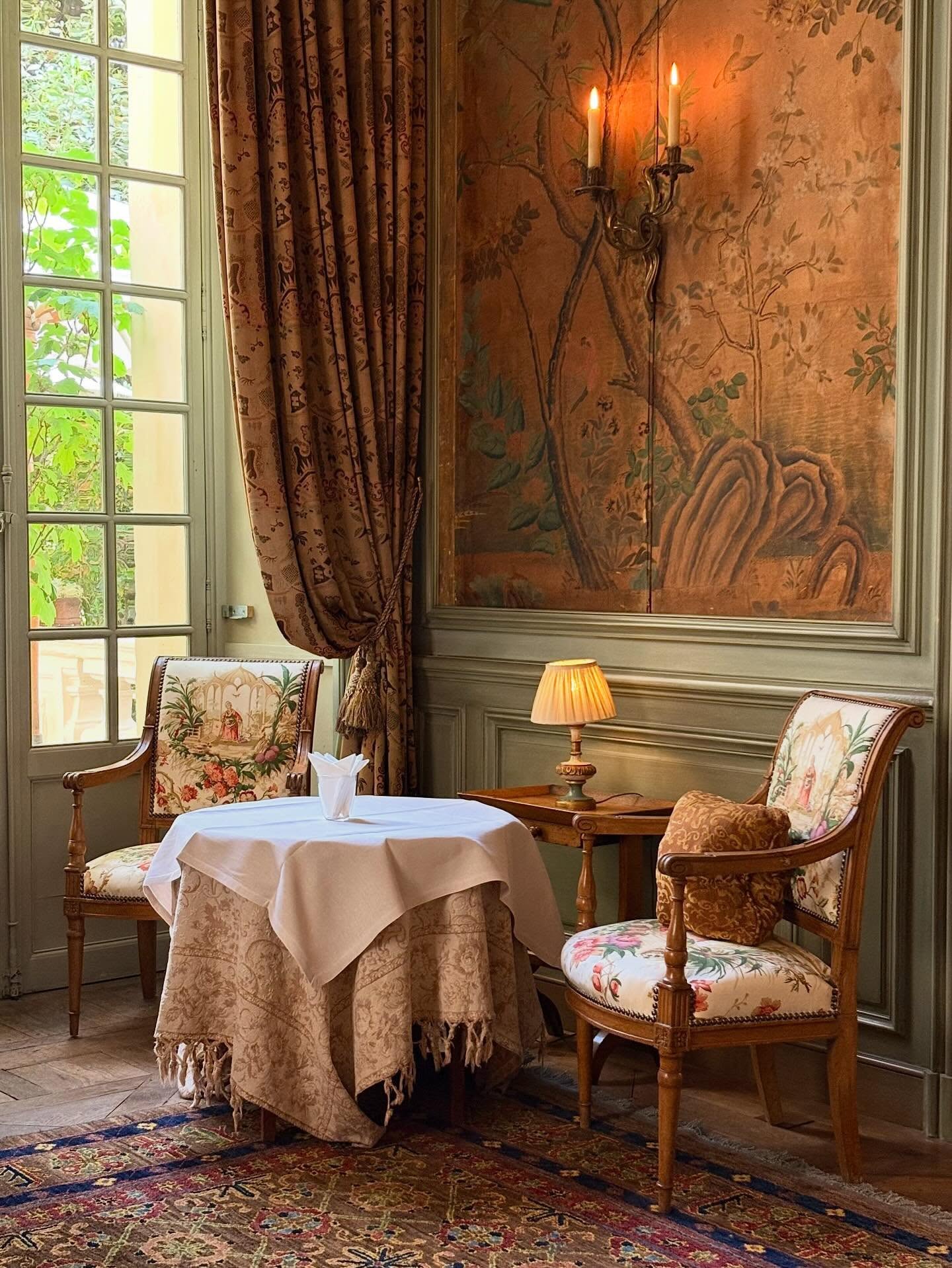 Intimate dining table framed by antique painted wallpaper and floral curtains at Hôtel La Mirande in Avignon.