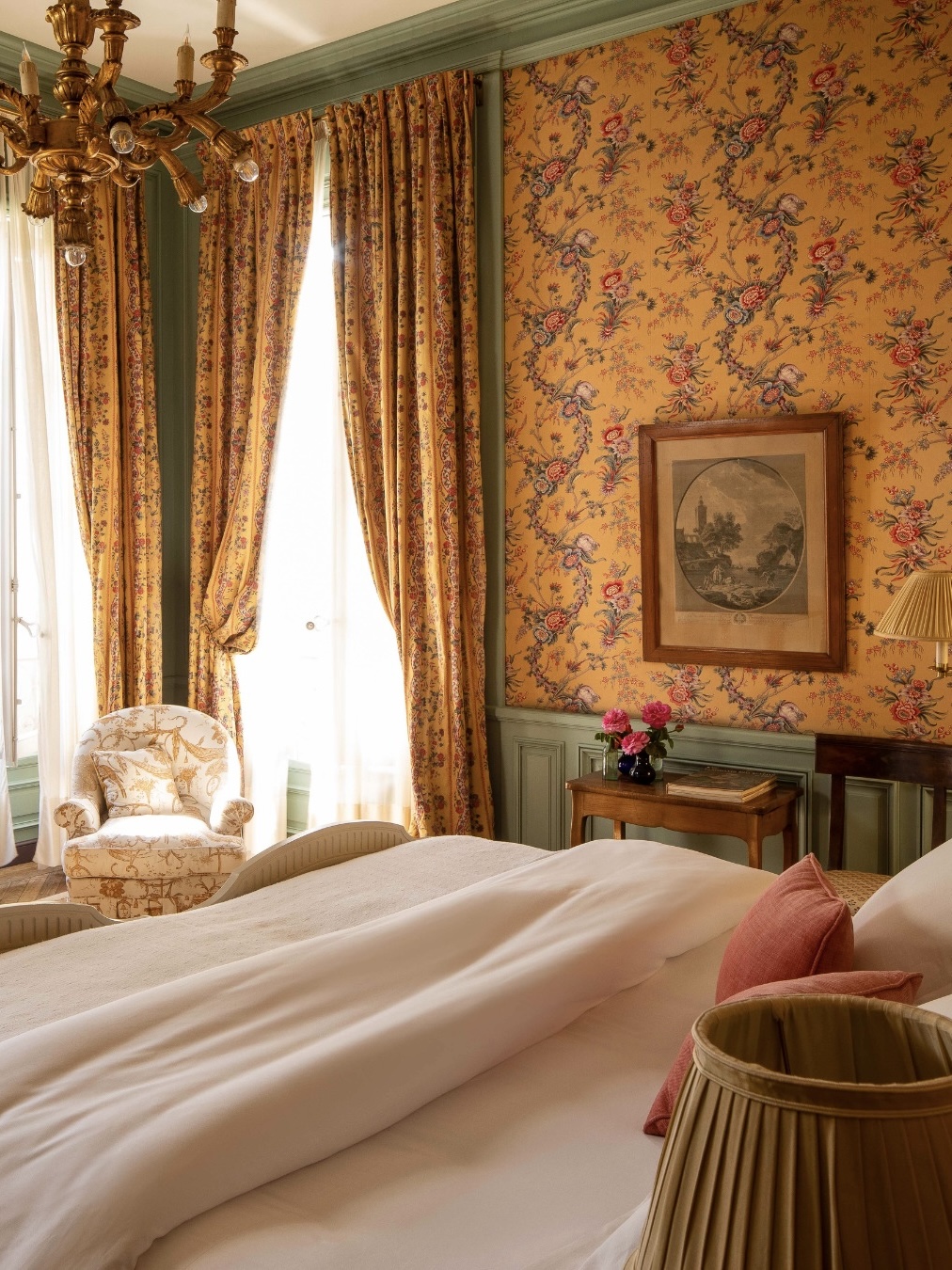 Luxury hotel room at Hôtel La Mirande with yellow patterned wallpaper, matching curtains, and a plush turned down bed.