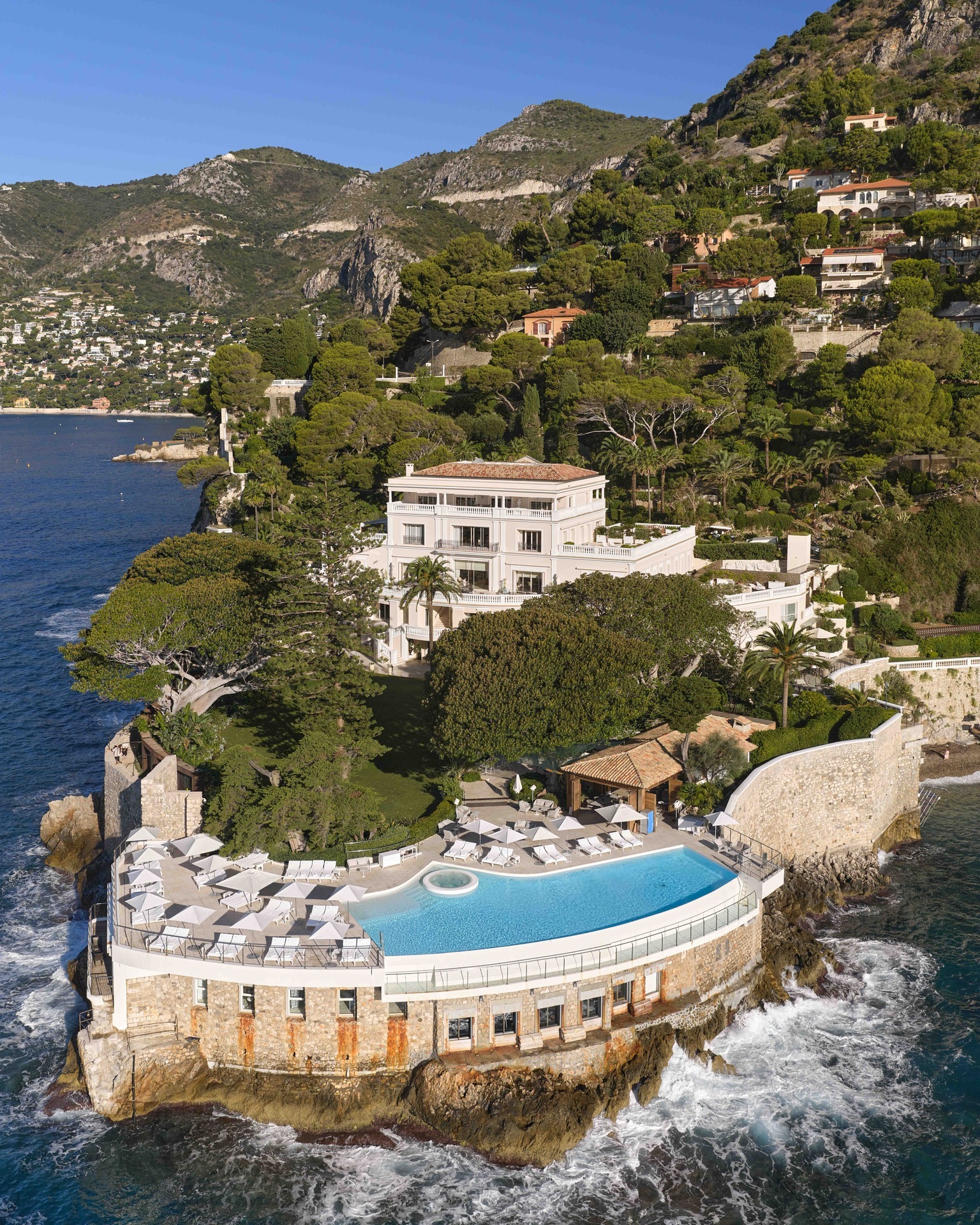 Cap Estel luxury hotel and swimming pool surrounded by lush green mountains, overlooking the Mediterranean Sea.