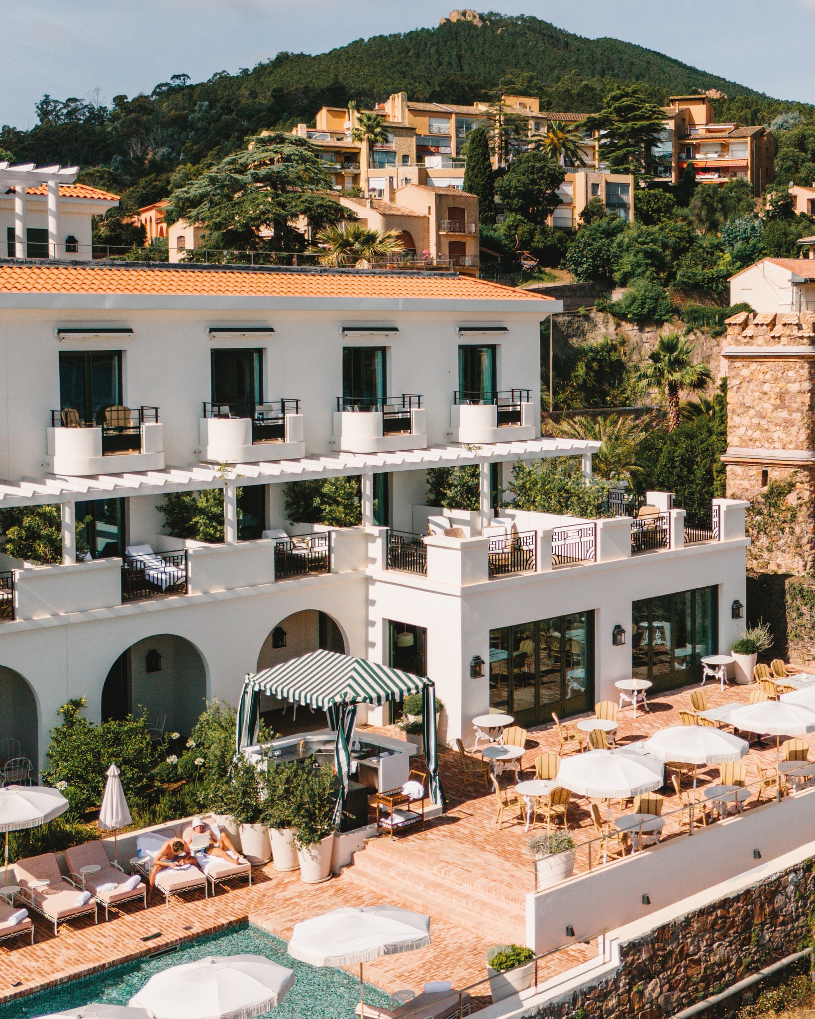 Chateau de Theoule hotel terrace and swimming pool featuring red brick and lounge chairs surrounded by natural lush greenery.