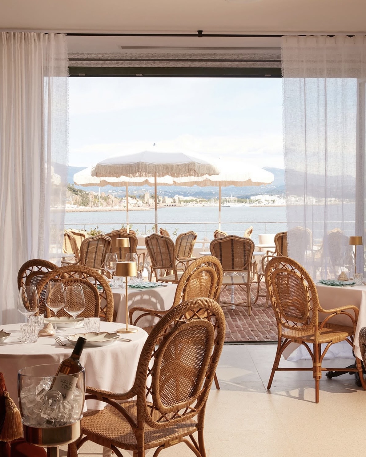 Chateau de Theouleopen hotel dining room and terrace with wicker chairs and intimate dining tables overlooking the Mediterranean Sea.