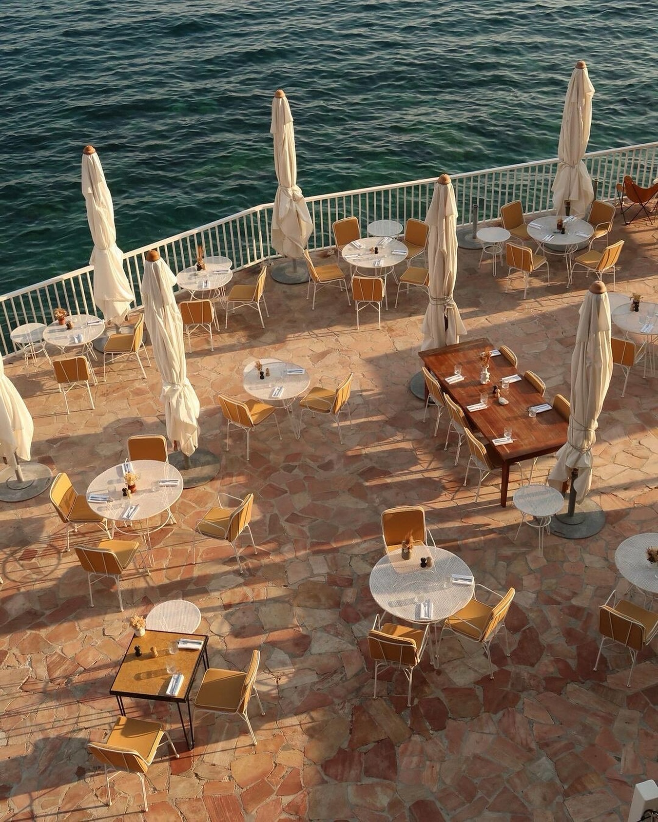 Roches Rouges hotel restaurant terrace with stone tiled floors, wood tables, and yellow chairs overlooking the Mediterranean Sea along the French Riviera.