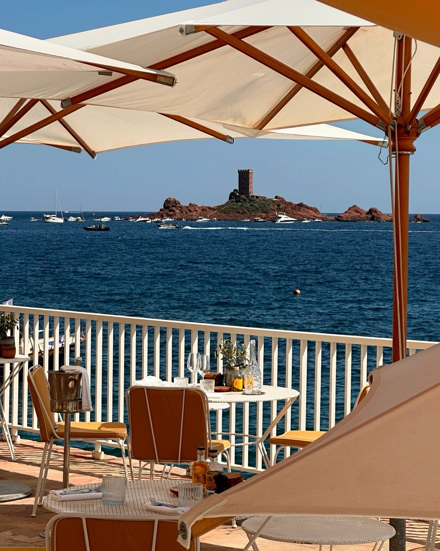 Roches Rouges hotel and restaurant terrace with intimate dining tables shaded by parasols overlooking the blue Mediterranean Sea.