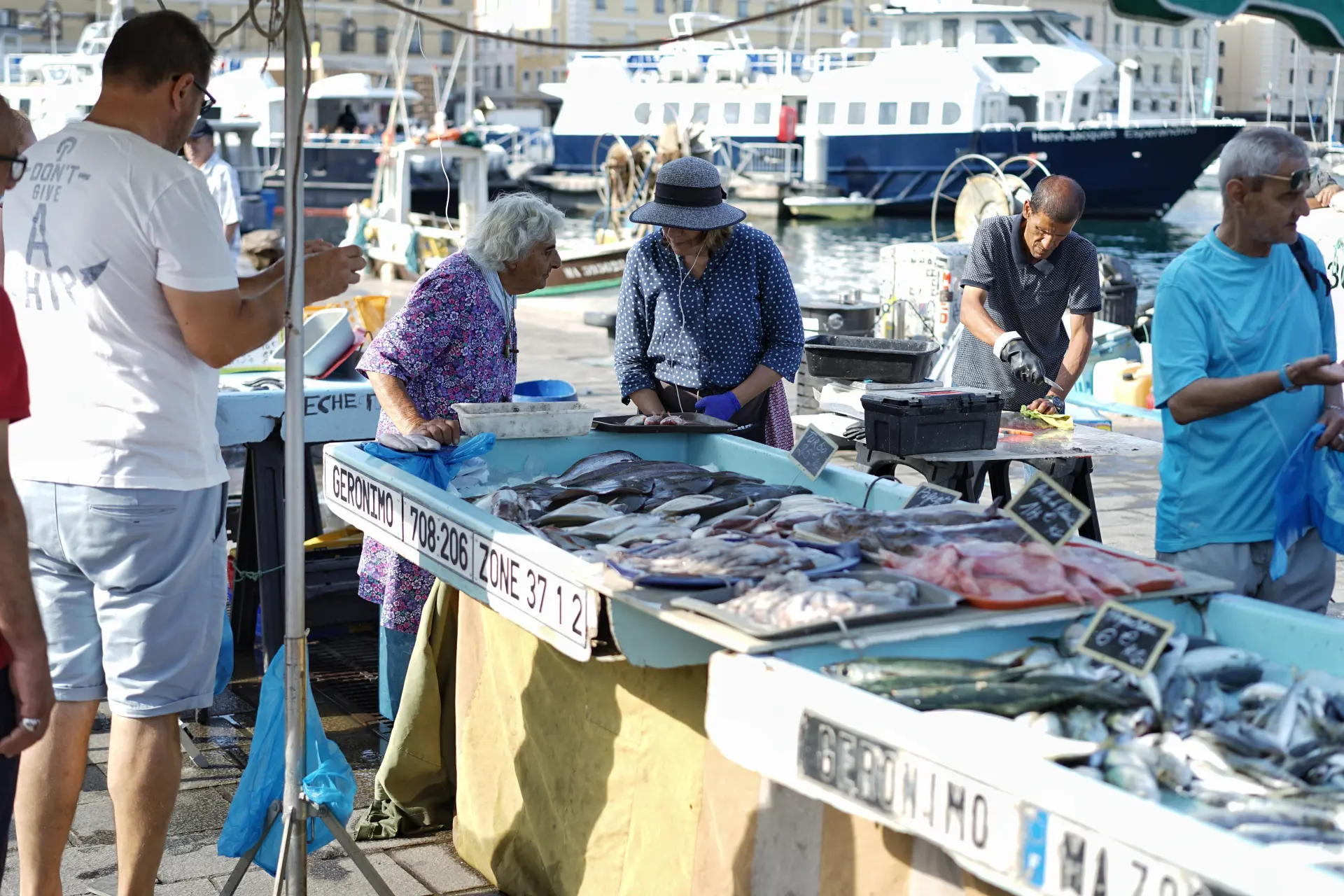 Open air fish market along the Old Port of Marseille with vendors and shoppers gathered around tables of locally caught seafood.