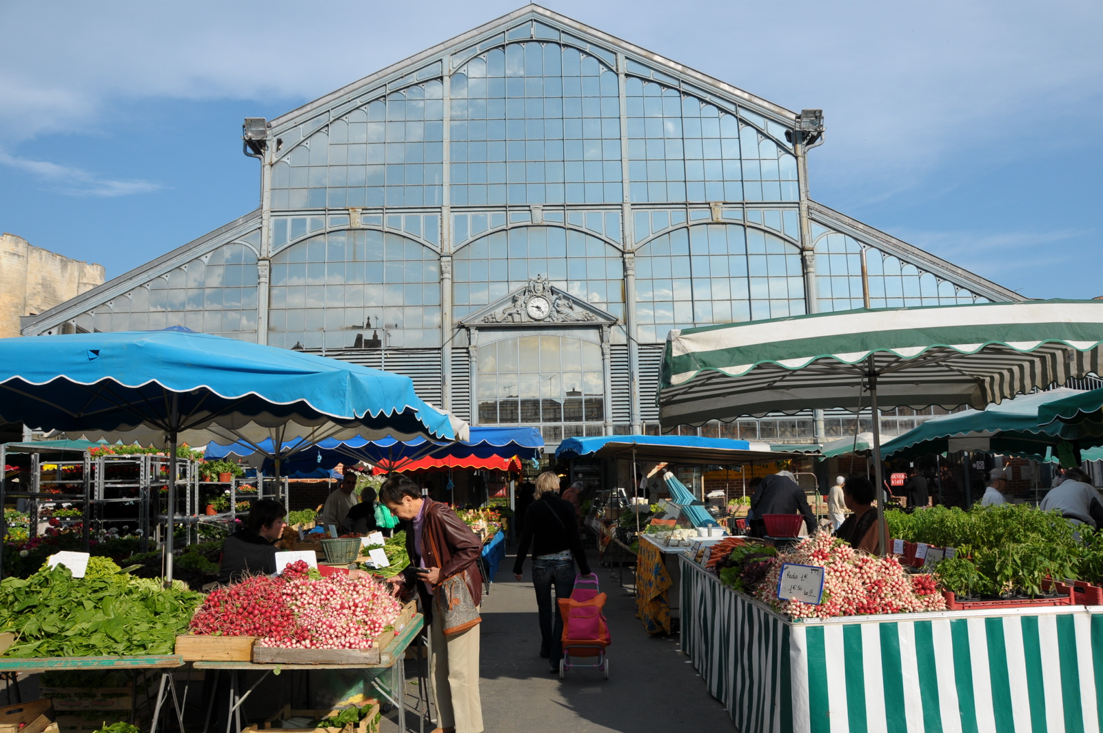 Piles of French radishes and salad greens at Les Halles de Niort market in front of a glass building.