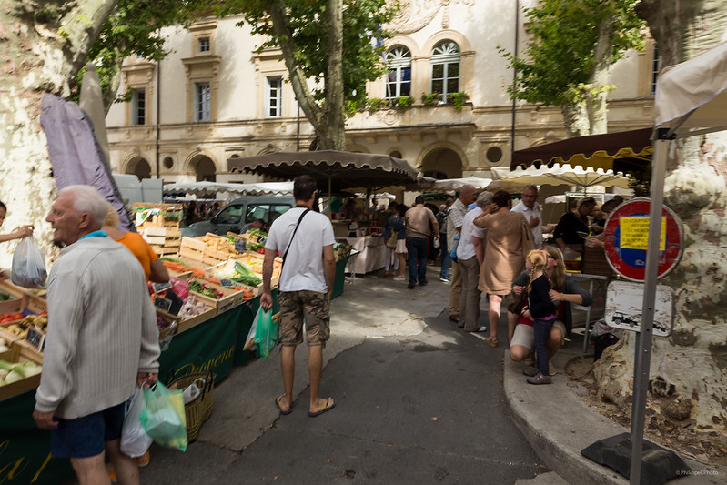 Le Marché de Saint-Rémy-de-Provence with market stalls and vendors offering fresh produce to pedestrians and shoppers.