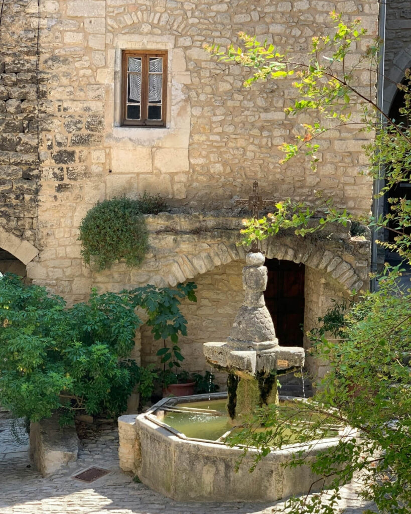 Garden courtyard in Provence, France featuring a central stone pond and fountain.