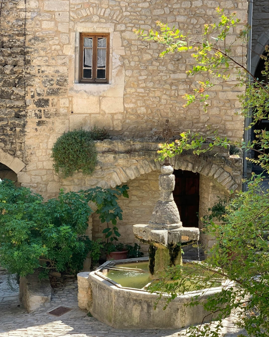 Garden courtyard in Provence, France featuring a central stone pond and fountain.