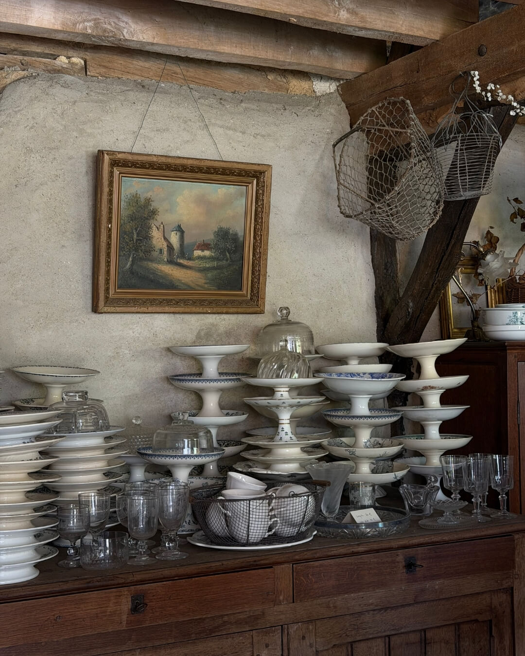 Antique china cake stands and crystal wine glasses stacked on a wood hutch at an Antique market in Normandy.