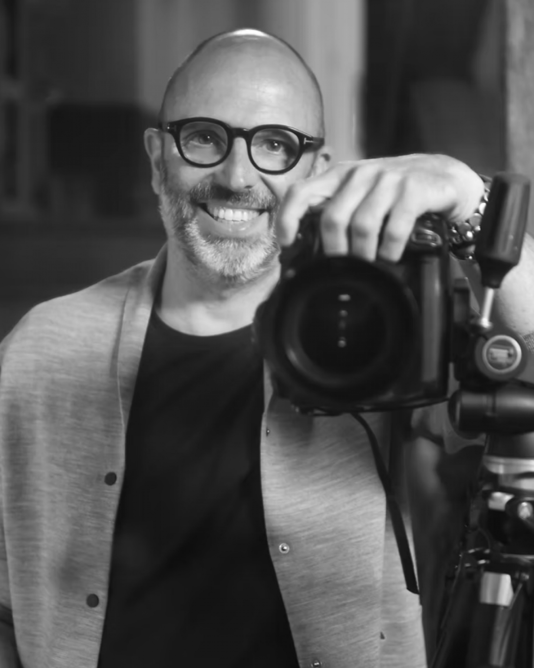 Man smiling while posing with a camera.