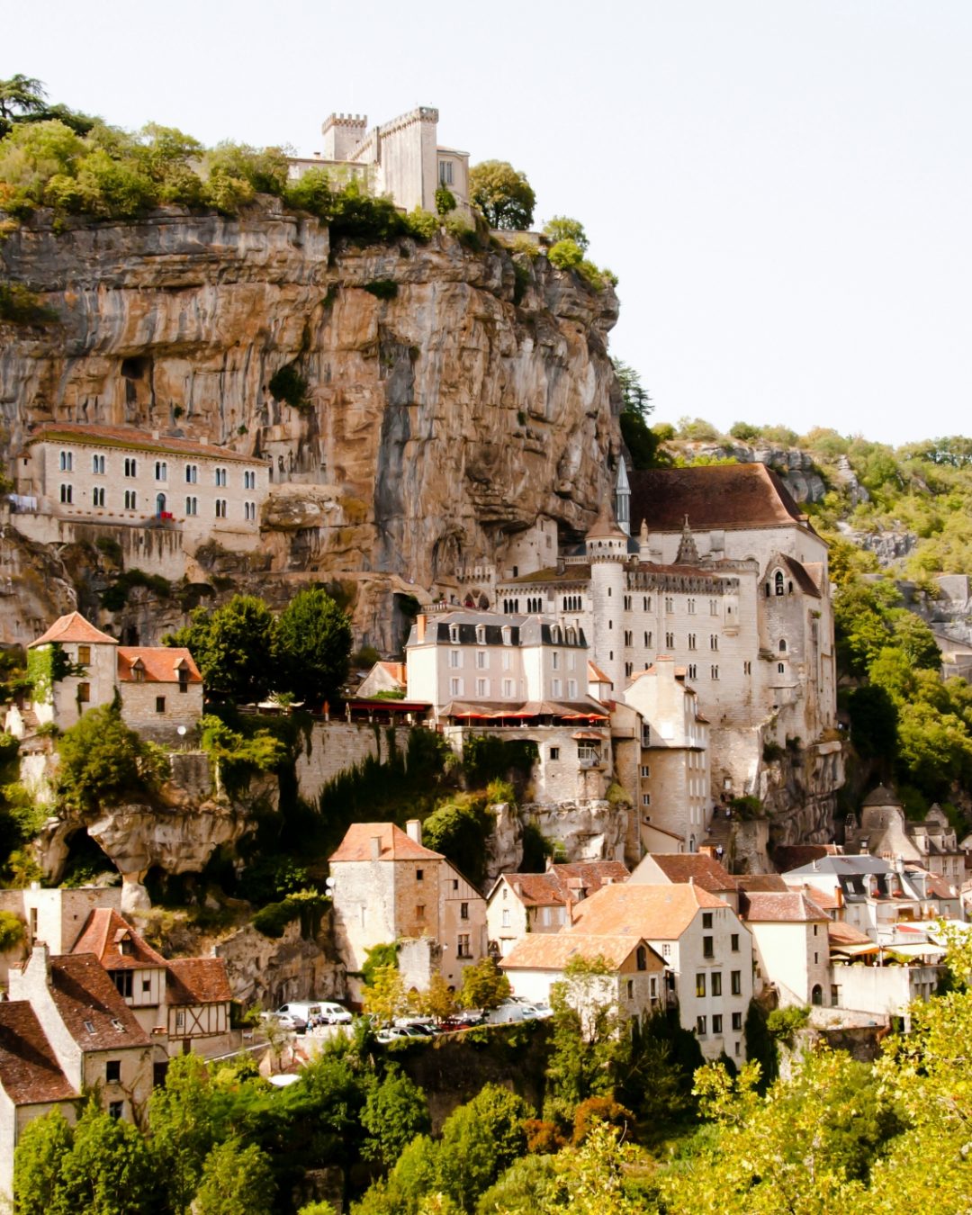 A mountainside village with homes clustered and stacked against a rugged cliff and surrounded by greenery.