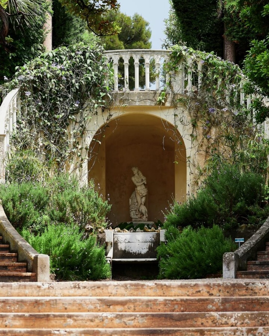 A stone statue framed by historic stone steps and lush greenery on the French Riviera.