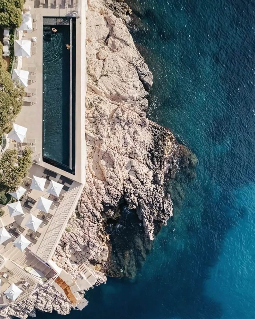 Aerial view of the Roches Blanches pool and the gem coloured Mediterranean Sea in Cassis, both glittering with vibrant blue hues.