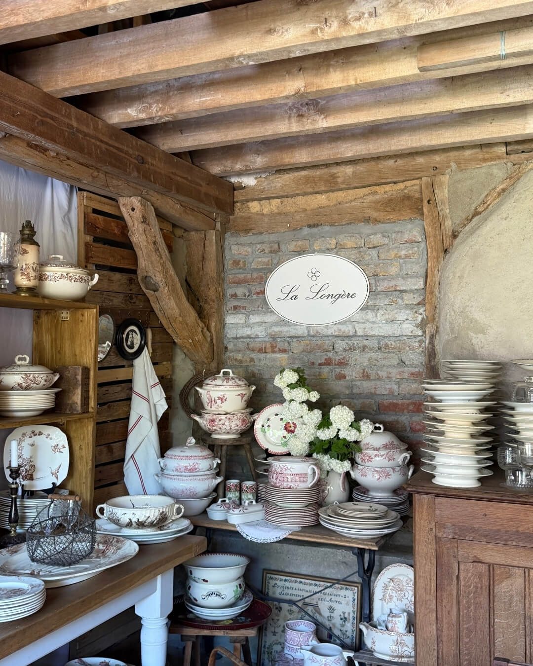 Antique dishes and soup tureens arranged on rustic wood tables at a market in Normandy.