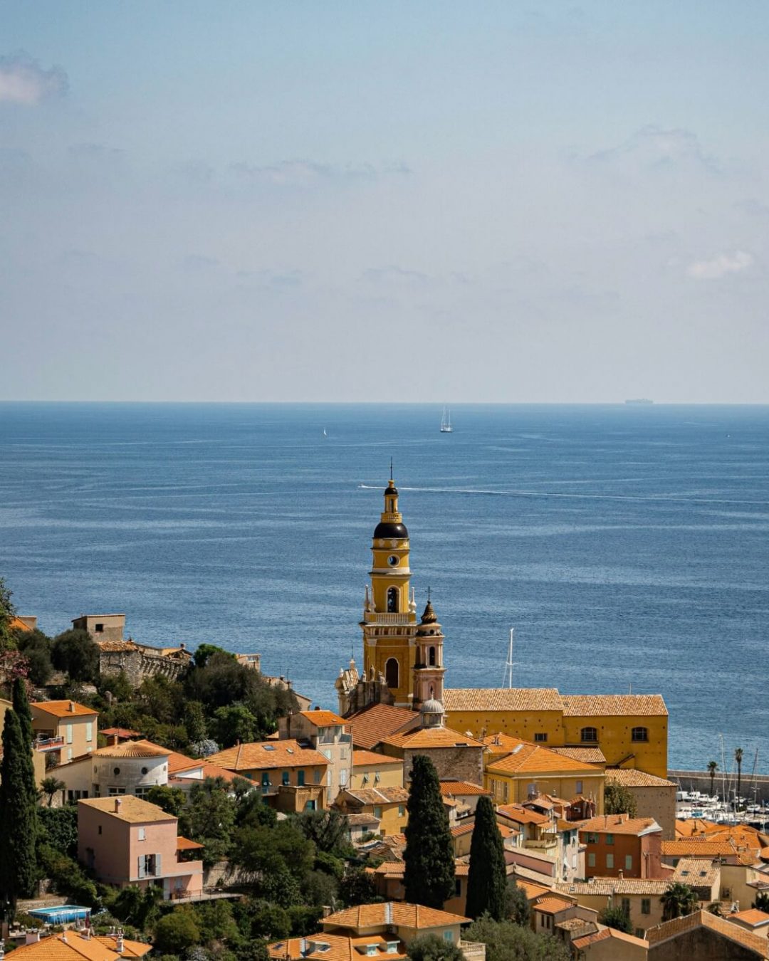 The French village of Menton on the French Riviera, overlooking the blue Mediterranean Sea with clear skies and boats in the distance.