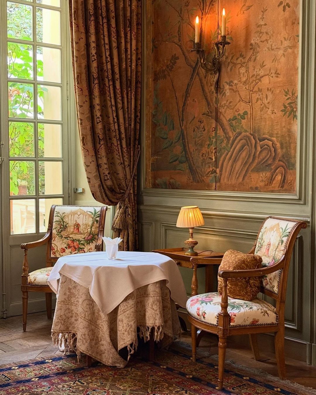Intimate dining table framed by antique painted wallpaper and floral curtains at Hôtel La Mirande in Avignon.